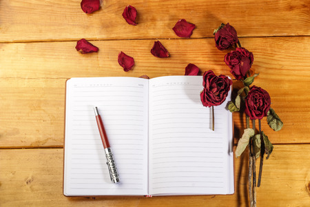 red dried roses with book and pen isolated on wooden backgroundの写真素材