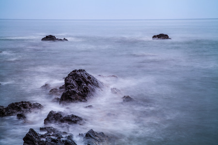 A slow shutter photo of moving waves hitting the shore and rocks on the beach.の写真素材