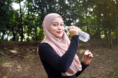 A pretty muslim woman athlete resting while drink a bottle of mineral waterの写真素材