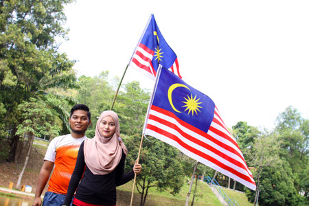 Cheerful couple friends  holding a nation flag for a Malaysia independence day with a happy reaction