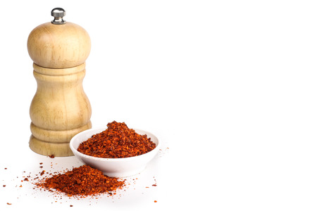 red chili flakes with grinder in the background isolated in whiteの写真素材
