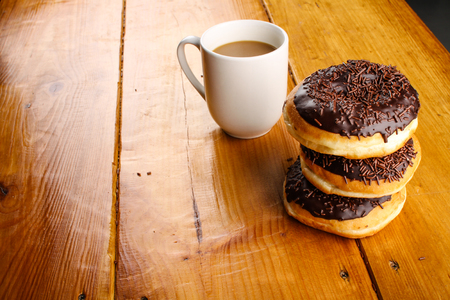 pile of chocholate doughnuts with a hot drink in wood backgroundの写真素材