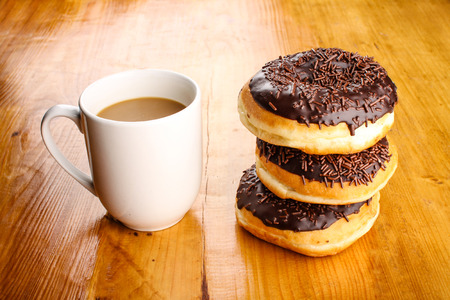 pile of chocholate doughnuts with a hot drink in wood backgroundの写真素材