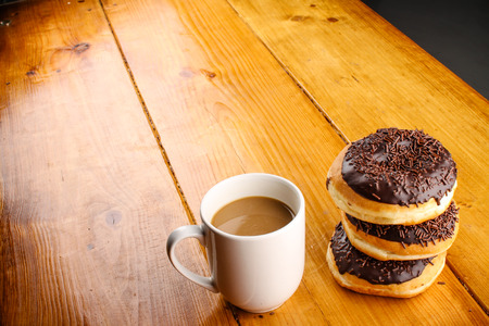 pile of chocolate doughnuts with a hot drink in wood backgroundの写真素材