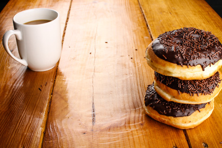 pile of chocolate doughnuts with a hot drink in wood backgroundの写真素材