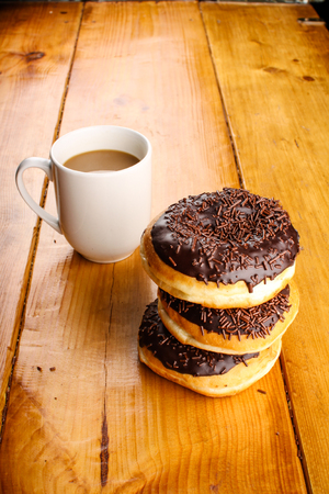 pile of chocolate doughnuts with a hot drink in wood backgroundの写真素材