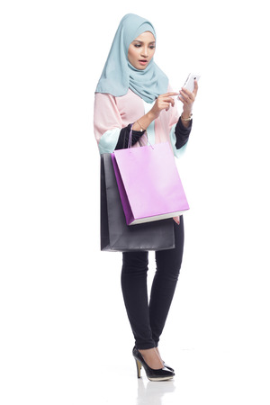 portrait of asian muslimah woman with her shopping bag having fun with toy camera in white backgroundの写真素材