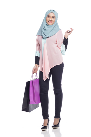 portrait of asian muslimah woman with her shopping bag having fun with toy camera in white backgroundの写真素材
