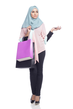 portrait of asian muslimah woman with her shopping bag having fun with toy camera in white backgroundの写真素材