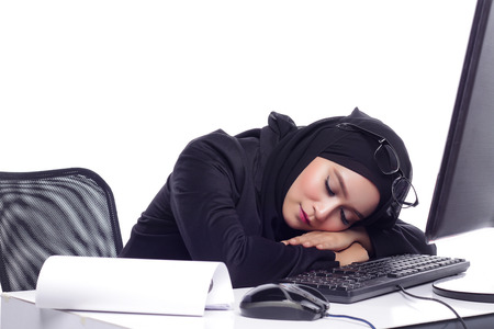 beautiful corporate muslimah woman with office attire showing tired expression while working on desktop computerの写真素材