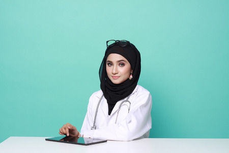 muslimah doctor holding a stethoscope isolated in turquoise  backgroundの写真素材