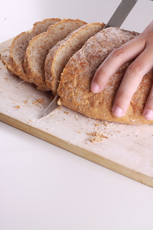 slicing a wheat bread on top of chopping board isolated in white backgroundの写真素材