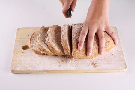 slicing a wheat bread on top of chopping board isolated in white backgroundの写真素材