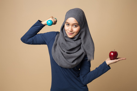 a young beautiful hijab woman holding dumbbells and apple on a yellow background.の写真素材