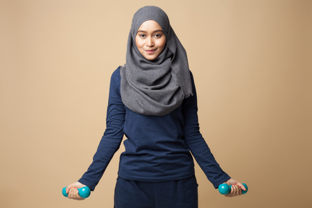 A young beautiful hijab woman is doing exercise with dumbbells on a yellow backgroundの写真素材