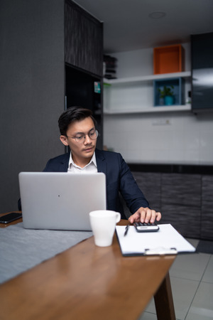 asian malay man working at home with laptop and calculatorの写真素材