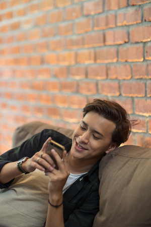 young asian chilling indoor with smartphoneの写真素材