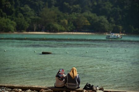 two asian muslim woman setting at the jetty and looking at the seaの写真素材