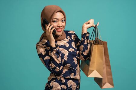 This woman is talk with phone while hold the bag. At Turquoise color backgroundの写真素材