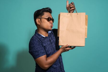 The guy kiss the bag he bought. At Turquoise color backgroundの写真素材