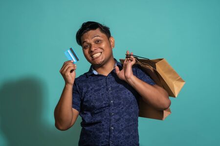 A guy who enjoys shopping with a credit card at turquoise background.の写真素材