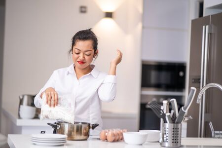 She pours flour into a bowl while smilingの写真素材