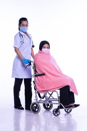 A feverish female patient sat in a wheelchair at a hospital with her doctor. On a white backgroundの写真素材