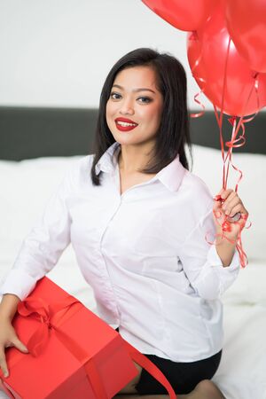 Beautiful young woman with balloons red and box on bed. Valentine's day celebrationの写真素材