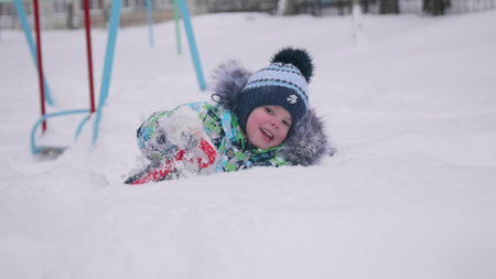 A little child playing with snow in winter Park. Lying and smiling baby on white fluffy snow. Fun and games in the fresh air.の写真素材