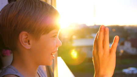 Young guy standing by the window in the morning. The first rays of the sun illuminate the room. The...