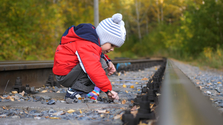 Lonely boy playing on the railroad tracks. Dangerous games and entertainment. Autumn warm day.の写真素材