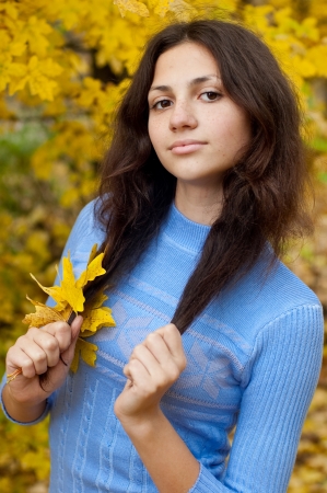 Beautiful young girl is by an autumn day with yellow maple leavesの写真素材