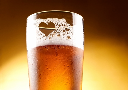 Glass of beer with the heart represented with froth close up over yellow backgroundの写真素材