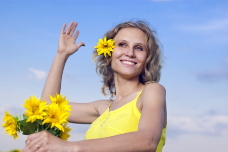 Beautiful young girl with sunflowers on a background cloudsの写真素材