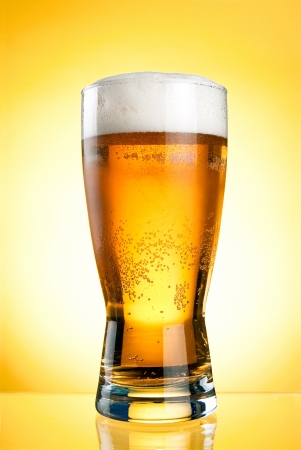 Glass of beer close-up with froth over yellow backgroundの写真素材