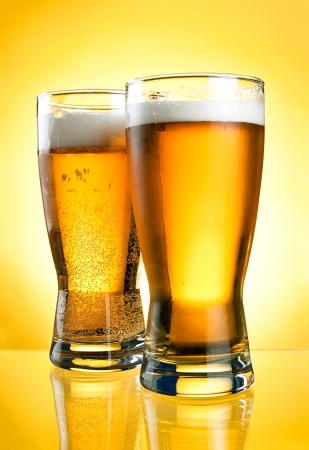 Two glasses of beer close-up with froth over yellow backgroundの写真素材
