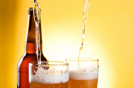 Beer Being Poured in Two glasses and Bottle on yellow backgroundの写真素材