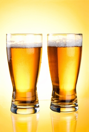 Two glasses of beer close-up with froth over yellow backgroundの写真素材