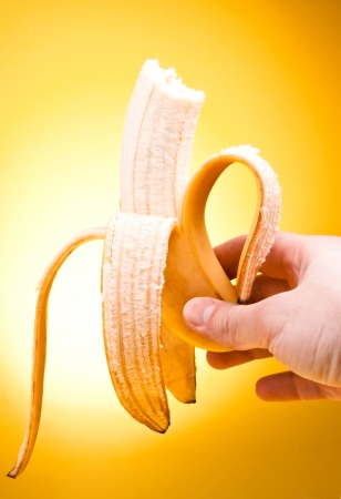 Hand holding peeled Bitten off  banana over yellow backgroundの写真素材