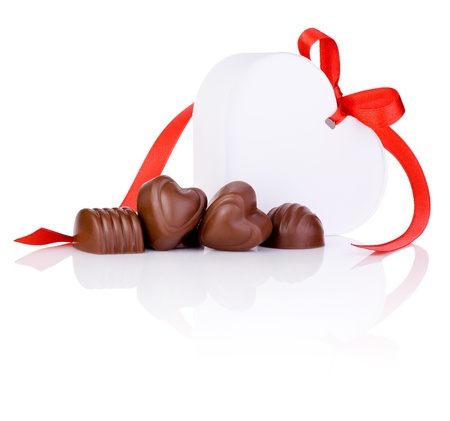 Chocolate candies and White gift in the form of heart with a bow of red ribbon Isolated on white backgroundの写真素材