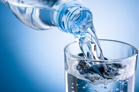 Pouring water from bottle into glass on blue backgroundの写真素材