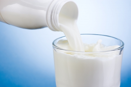 Pouring milk from white plastic bottle into glass on blue backgroundの写真素材