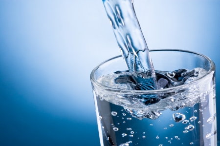 Pouring water into glass on blue backgroundの写真素材