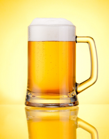Mug fresh beer with cap of foam isolated over yellow backgroundの写真素材
