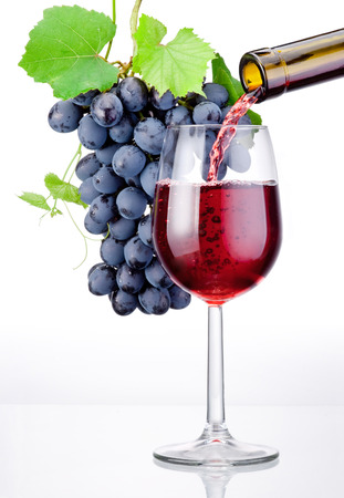 Pouring a glass of red wine and bunch of grapes with leaves isolated on white backgroundの写真素材