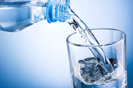 Close-up pouring water from bottle into glass on a blue backgroundの写真素材