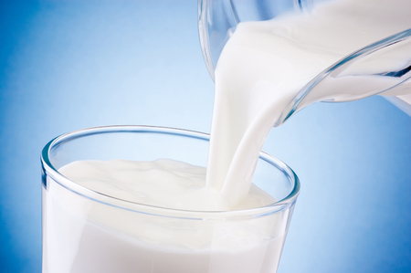 Pouring fresh milk into glass from jug on a blue backgroundの写真素材