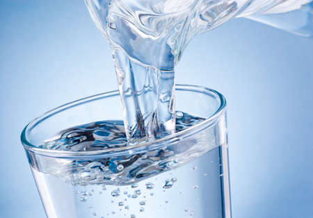 Water poured from jug into glass on a blue backgroundの写真素材
