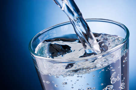 Water pouring into glass on a blue backgroundの写真素材