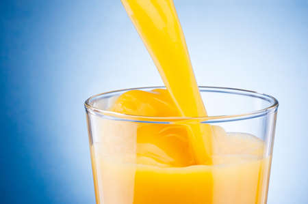 Orange juice pouring into glass on a blue backgroundの写真素材